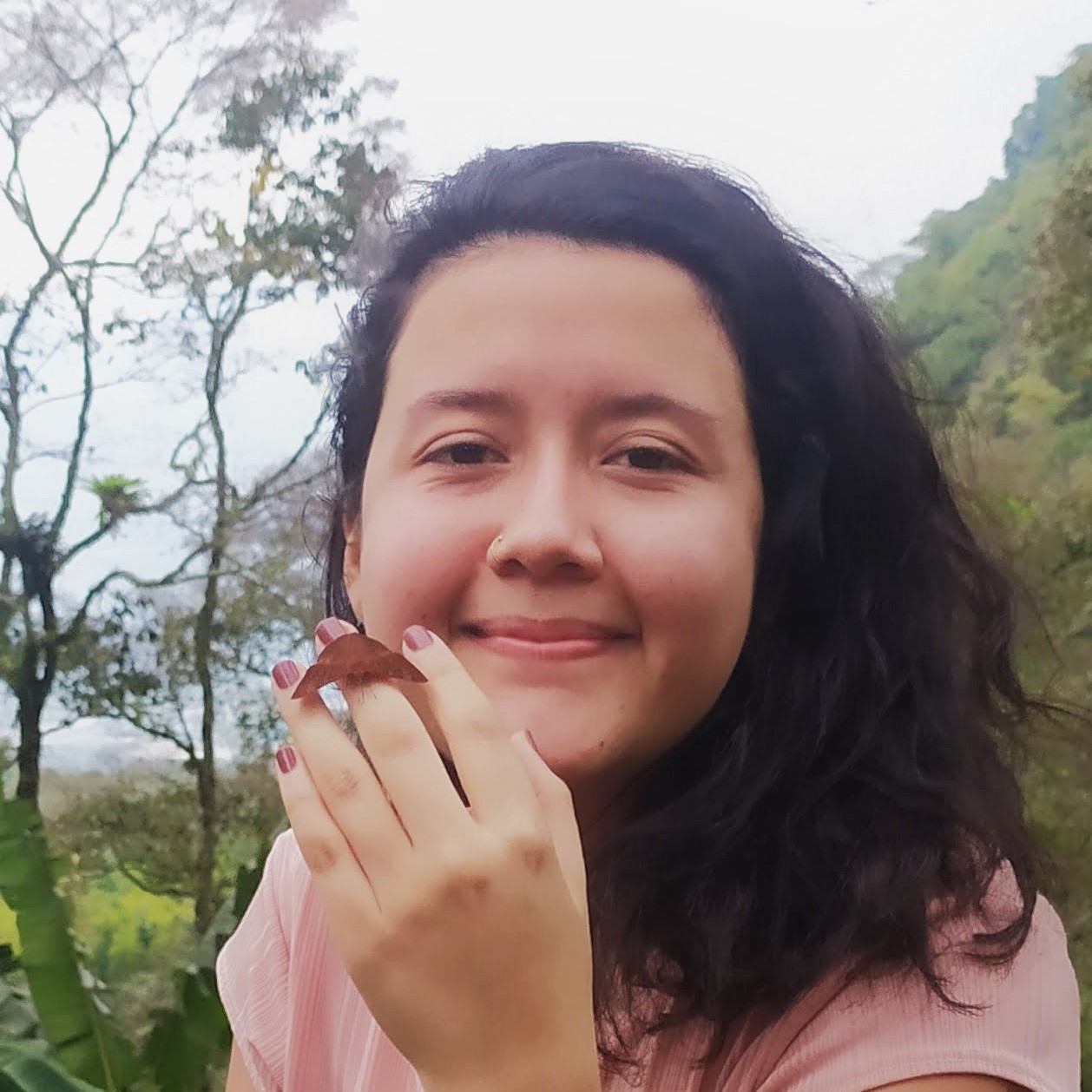 Laura Sierra-Botero in foggy mountains holding a brown moth up to her face and smiling at the camera.